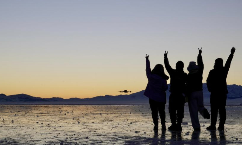 Tourists take photos with a drone on the frozen surface of Sayram Lake at sunset in Bortala Mongolian Autonomous Prefecture, northwest China's Xinjiang Uygur Autonomous Region, Jan. 13, 2025. Sayram Lake is the largest and highest alpine lake in Xinjiang. (Xinhua/Du Juanjuan)