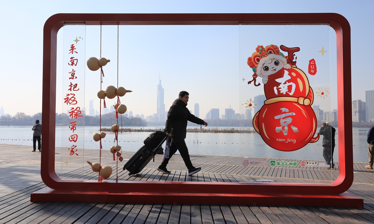 A passenger with luggage walks past a display window decorated with Spring Festival elements set up by Xuanwu Lake near Naijing Station, in Nanjing, East China's Jiangsu Province on January 17, 2024. Photo: VCG