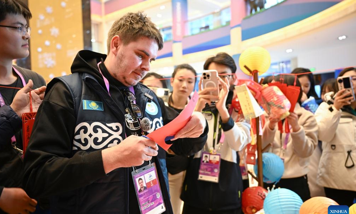A journalist from Kazakhstan tries paper cutting at an activity to celebrate the Lantern Festival at press center for the 9th Asian Winter Games in Yabuli, northeast China's Heilongjiang Province, Feb. 12, 2025. (Xinhua/Hu Huhu)