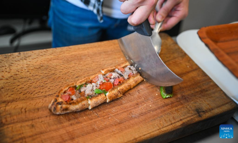 A waiter cuts the baked pide at a restaurant in Bursa, Türkiye, April 17, 2025. Pide is a traditional Turkish dish that originated in the Black Sea region and is now popular throughout Türkiye. It is usually flat and narrow in shape, with meat, cheese, vegetables and other fillings baked in a stove. (Xinhua/Liu Lei)