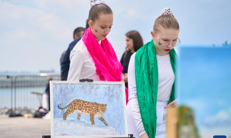 People walk past an oil painting of Far Eastern leopard during a 