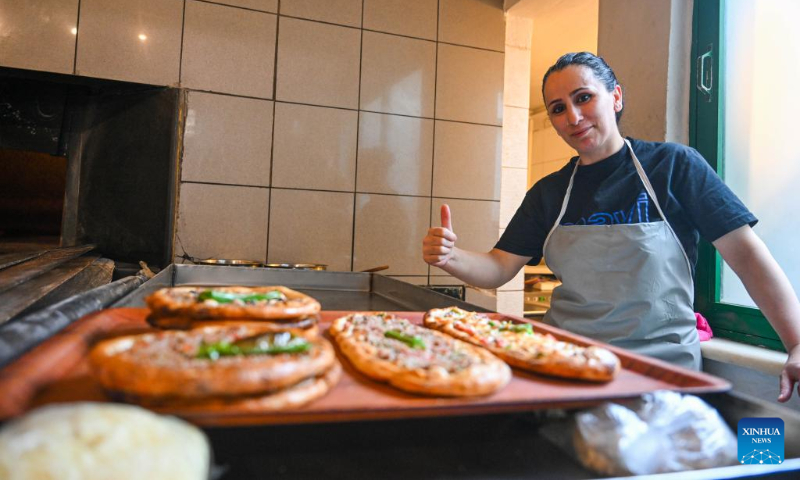 A waiter poses behind prepared pides at a restaurant in Bursa, Türkiye, April 17, 2025. Pide is a traditional Turkish dish that originated in the Black Sea region and is now popular throughout Türkiye. It is usually flat and narrow in shape, with meat, cheese, vegetables and other fillings baked in a stove. (Xinhua/Liu Lei)