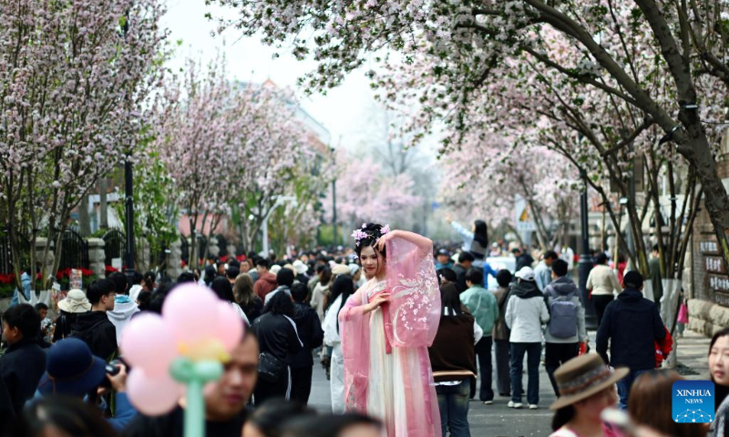 A tourist in traditional Chinese costume poses for photos at the Wudadao historical urban area in north China's Tianjin, April 4, 2025. The third edition of a crabapple blossom festival kicked off on Thursday at Wudadao historical urban area, a popular tourist destination in the downtown area of Tianjin. The festival, which stays on until April 13, features more than 100 art and culture performances to enable 