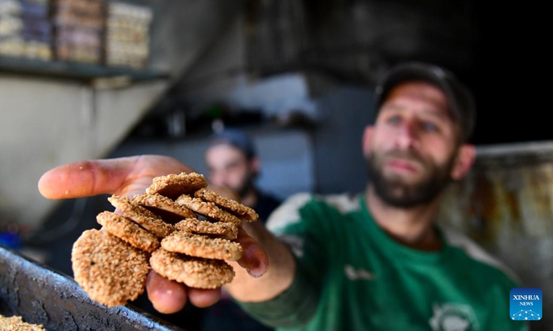 A man shows freshly baked sesame cookies at a traditional sweets shop in the old market of Damascus, Syria, on March 27, 2025. As Eid al-Fitr approaches, bakeries across Damascus are busy preparing maamoul and other confections made with wheat flour and stuffed with pistachios, walnuts or dates. (Photo: Xinhua)