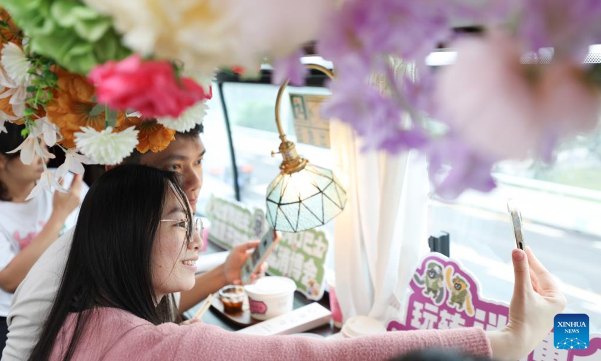 Tourists take photos on the Laobacha Haikou Bus's China International Consumer Products Expo special route in Haikou, south China's Hainan Province, April 6, 2025. Ahead of the upcoming fifth China International Consumer Products Expo (CICPE), the Laobacha Haikou Bus has inaugurated its CICPE special route. Laobacha is a beloved Hainan tradition where locals gather over fragrant tea, savory snacks, and leisurely chat.  (Photo: Xinhua)