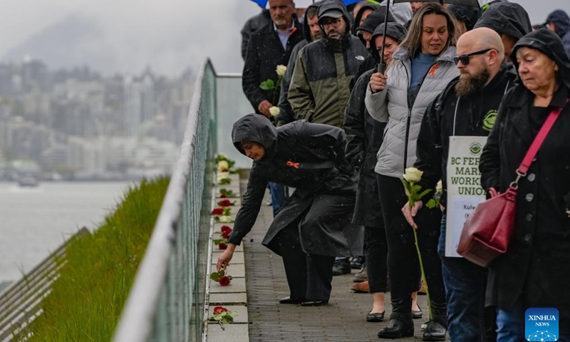 A woman places a rose in front of a memorial glass panel during the National Day of Mourning event in Vancouver, British Columbia, Canada, on April 28, 2025. The National Day of Mourning is observed annually in Canada on April 28 to commemorate people who have lost their lives, suffered injury or illness on the job, or experienced a work-related tragedy, and to raise awareness of health and safety in the workplace. (Photo: Xinhua)