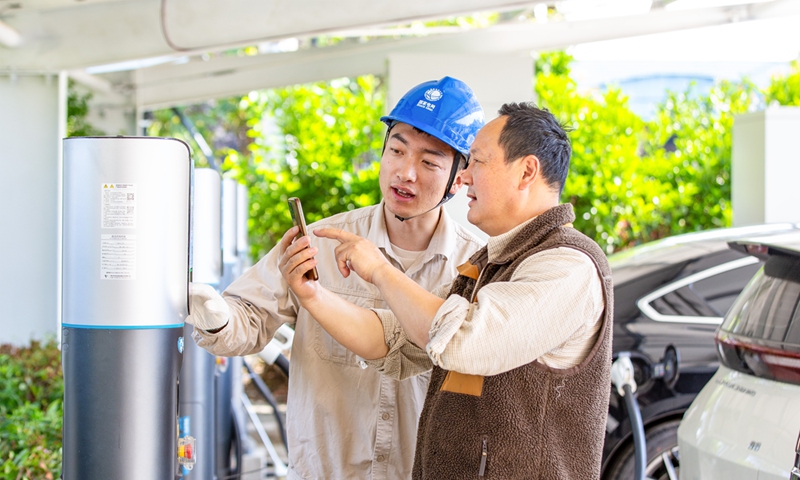 An electric power service worker helps a car owner to charge a new-energy vehicle by scanning codes on a cellphone at a 