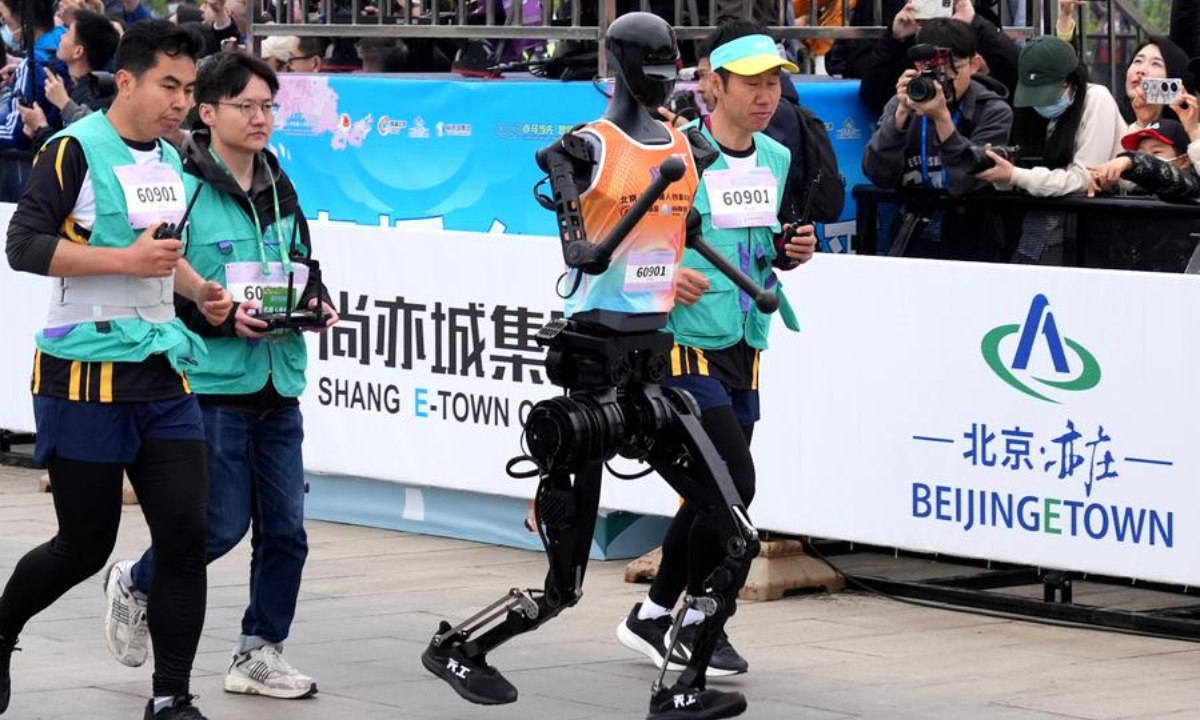 Robotic participant Tiangong Ultra (3rd L) competes as engineers run alongside during the Beijing E-Town half-marathon and humanoid robots half-marathon in the Beijing Economic-Technological Development Area in southeast Beijing, China, April 19, 2025. (Xinhua/Zhang Chenlin)