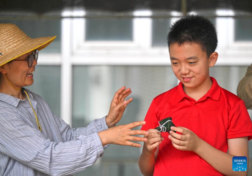 A volunteer teaches a child to make zongzi, a traditional Chinese food to mark the Dragon Boat Festival, at Huiai Farm in Yangliuqing Town, Xiqing District, north China's Tianjin, May 31, 2025. Huiai Farm covers an area of approximately 80 mu (about 5.33 hectares) and was jointly initiated and built by 8 families, whose children were diagnosed with autism or intellectual disabilities. (Xinhua)