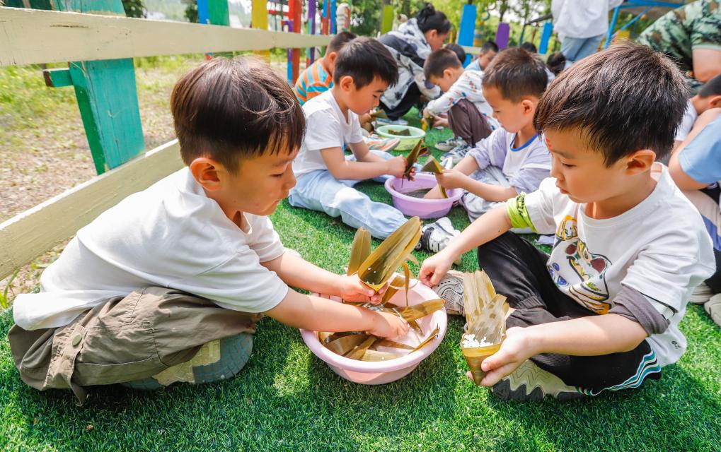 Children try their hands at making zongzi, a traditional Chinese food to mark the Dragon Boat Festival, at a nature education base in Xiaochang Township of Zunhua City, north China's Hebei Province, on May 30, 2025. The Dragon Boat Festival, also known as Duanwu Festival, is a traditional Chinese holiday to commemorate ancient Chinese poet Qu Yuan from the Warring States Period (475-221 B.C.). Celebrated on the fifth day of the fifth month of the Chinese lunar calendar, the festival falls on May 31 this year. (Photo by Liu Mancang/Xinhua)