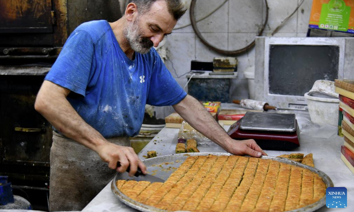 A baker cuts a large tray of baklava at a traditional sweets shop ahead of Eid al-Adha in Damascus, Syria, on June 4, 2025. Traditional sweets are widely prepared and exchanged during Eid celebrations. (Photo by Ammar Safarjalani/Xinhua)