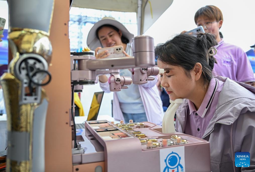 A visitor tries a make-up robot during the world robot carnival in Wuhan, central China's Hubei Province, June 2, 2025. The event kicked off here on Monday, featuring nearly 100 robots including pet robots, make-up robots, robotics band, etc. People interacted with the robots to experience the charm of technology-empowered life. (Xinhua/Du Zixuan)