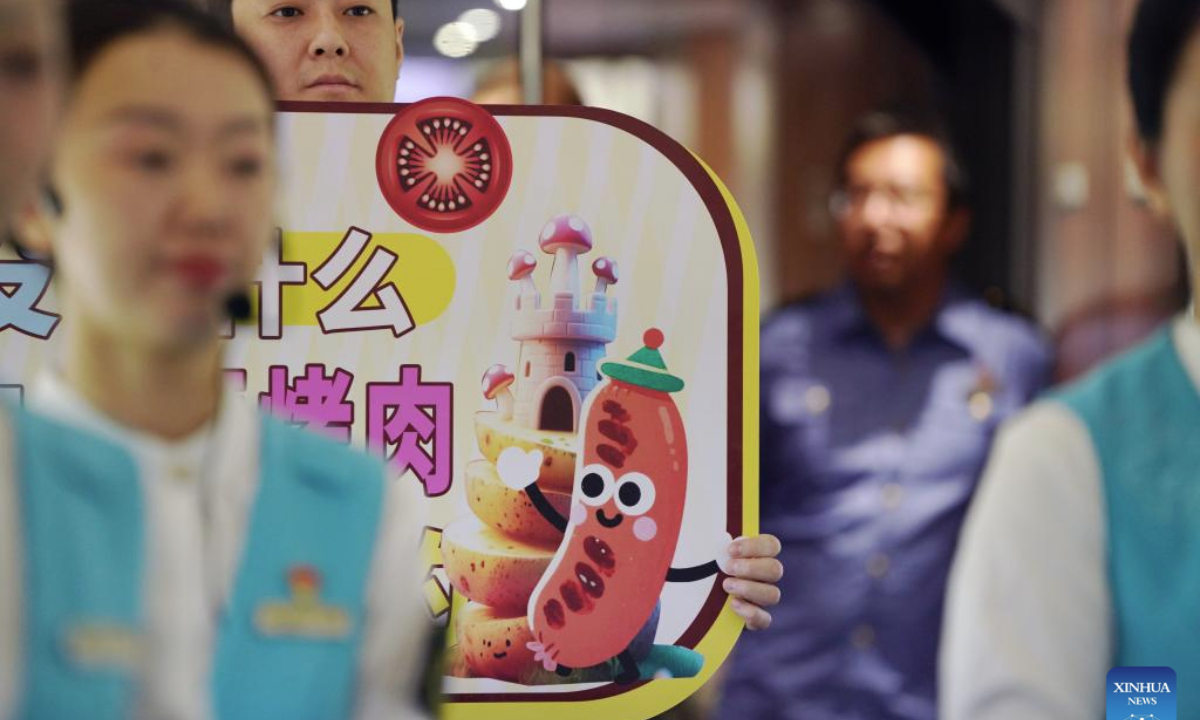 A steward shows a cartoon image of Qiqihar barbecue on train D6993 in northeast China's Heilongjiang Province, June 18, 2025. A Qiqihar barbecue cultural experiencing event was held Wednesday on bullet train D6993 running from Harbin West Railway Station to Qiqihar South Railway Station in Heilongjiang Province, offering a rich travel experience to passengers during the journey. (Xinhua/Wang Song)