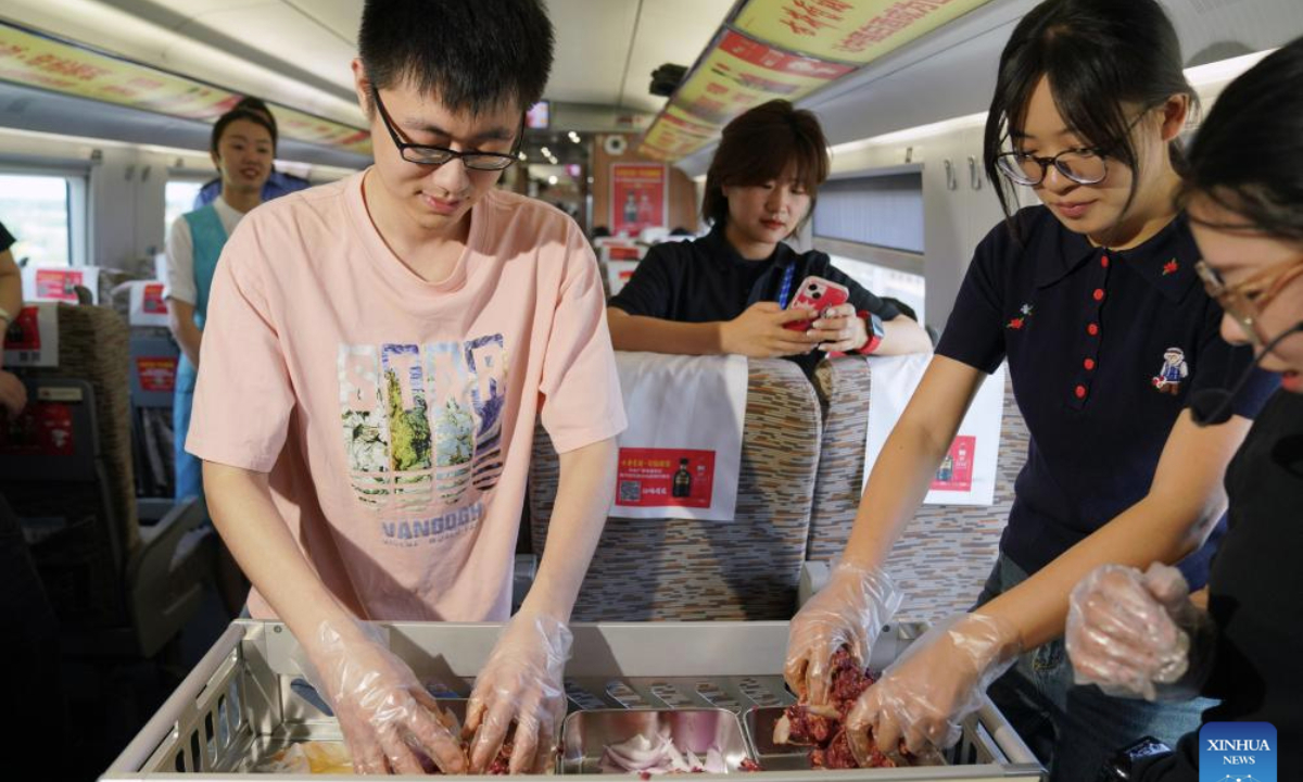 A passenger (L) tries to prepare Qiqihar barbecue on train D6993 in northeast China's Heilongjiang Province, June 18, 2025. A Qiqihar barbecue cultural experiencing event was held Wednesday on bullet train D6993 running from Harbin West Railway Station to Qiqihar South Railway Station in Heilongjiang Province, offering a rich travel experience to passengers during the journey. (Xinhua/Wang Song)