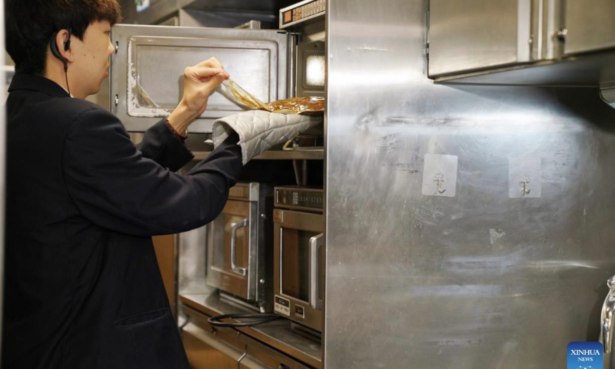 A steward heats Qiqihar barbecue on train D6993 in northeast China's Heilongjiang Province, June 18, 2025. A Qiqihar barbecue cultural experiencing event was held Wednesday on bullet train D6993 running from Harbin West Railway Station to Qiqihar South Railway Station in Heilongjiang Province, offering a rich travel experience to passengers during the journey. (Xinhua/Wang Song)