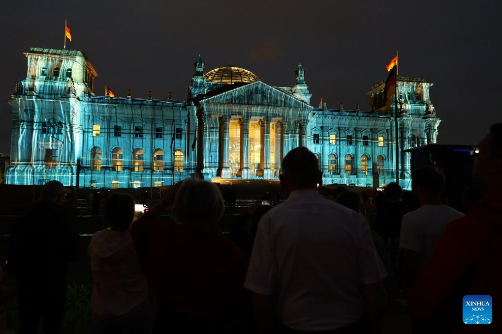 Visitors watch the illuminated Reichstag in Berlin, Germany, June 15, 2025. In the midsummer nights of Berlin, the Reichstag is once again wrapped, not in fabric this time, but in light. From June 9 to June 20, 24 synchronized projectors illuminate the building's west facade, simulating the visual effect of massive fabric wrapping and unveiling. The light show is designed to commemorate the 30th anniversary of Bulgarian-born artist Christo and his wife Jeanne-Claude's iconic 1995 artwork, Wrapped Reichstag. (Photo: Xinhua)