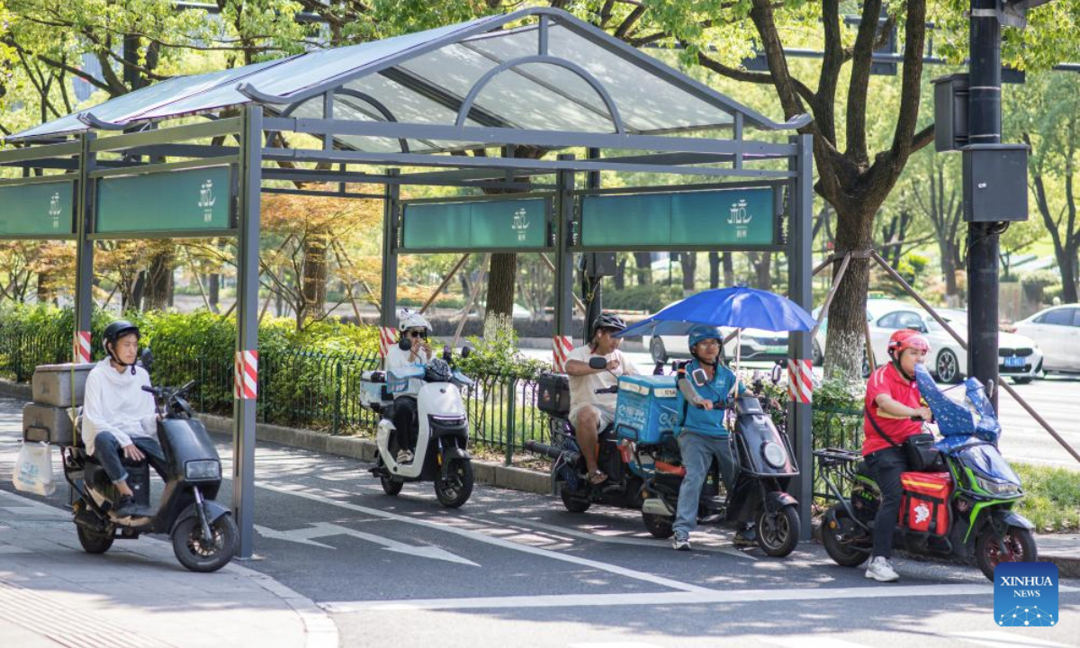 Riders wait for traffic light under a shelter in Hangzhou, east China's Zhejiang Province, July 3, 2025. Hangzhou issued an orange heat alert on Thursday. (Xinhua/Jiang Han)