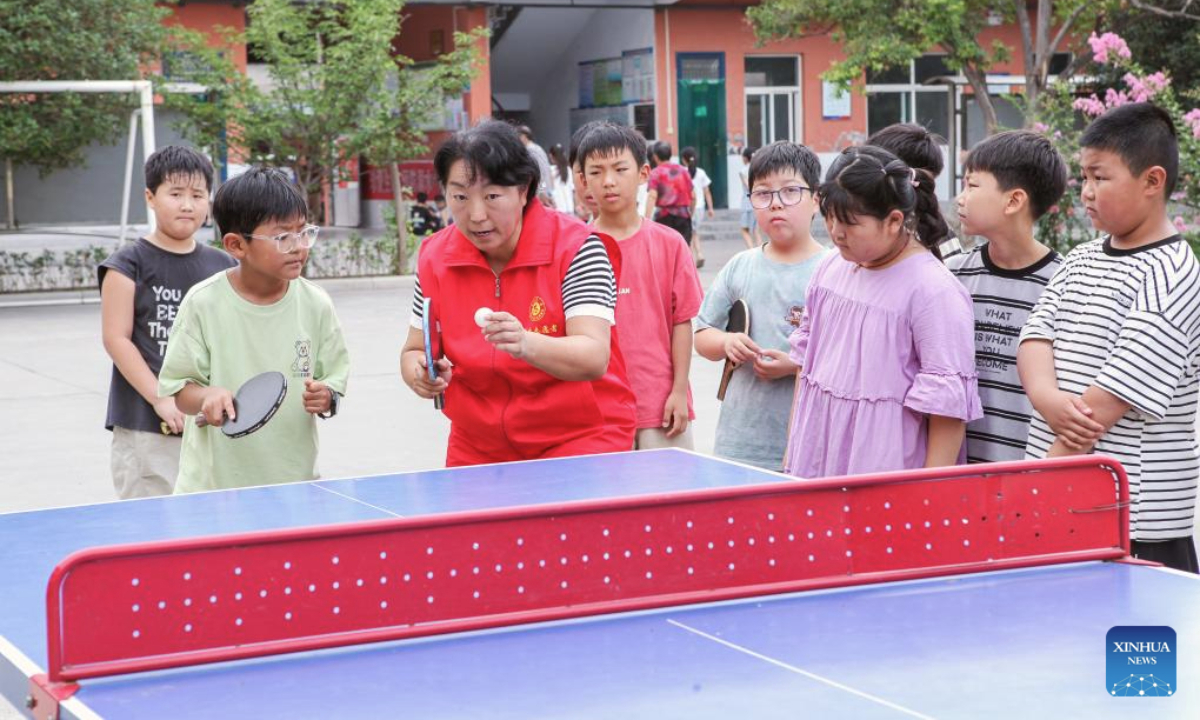 A volunteer instructs students to play table tennis at a children's palace in Jiaozuo City, central China's Henan Province, July 8, 2025. Children across the country are enriching their summer vacations through colorful activities. (Photo by Cheng Quan/Xinhua)