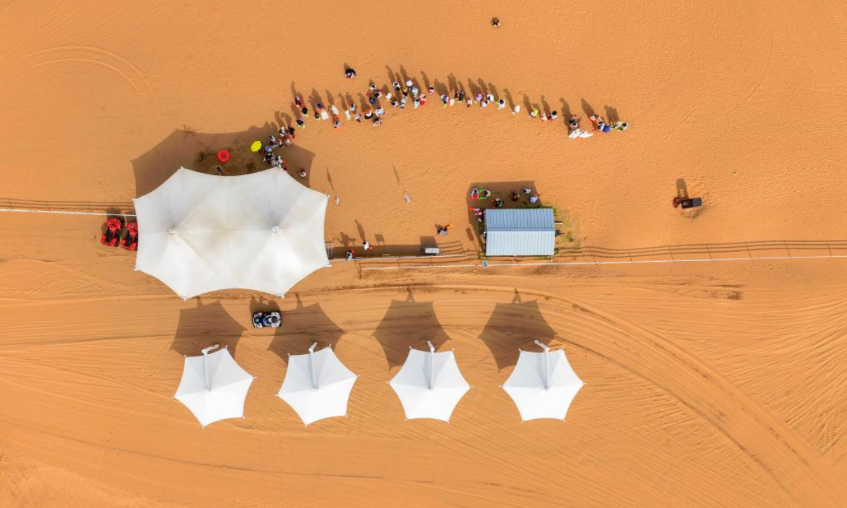 An aerial drone photo taken on Aug. 1, 2025 shows people queuing up to experience desert off-roading at a desert scenic area in Dalad Banner of Erdos City, north China's Inner Mongolia Autonomous Region. Kubuqi desert in Erdos City has entered its peak tourist season in midsummer, attracting numerous tourists from around the country to visit. (Xinhua/Lian Zhen)