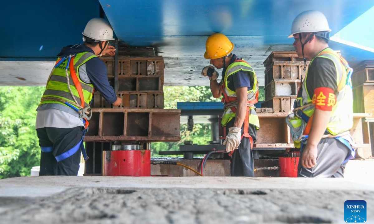 Workers work at the incremental launching construction site of a bridge of the Xi'an-Chongqing high-speed railway over an expressway in Dazhou, southwest China's Sichuan Province, July 11, 2025. The main body of a bridge of Xi'an-Chongqing high-speed railway over an expressway linking Yingshan and Dazhou in Sichuan Province was smoothly lowered onto its piers on Friday. This marks the successful completion of the incremental launching construction for China's first large-span high-speed railway network arch bridge with tied girders, laying a solid foundation for the timely opening of the Xi'an-Chongqing high-speed railway. The bridge spans 443.1 meters in total length, and the constructed tied-arch bridge section weighs 2,600 tonnes, measuring 147 meters long and 17 meters wide, with an incremental launching displacement of approximately 146 meters over a 10-day construction period. (Xinhua/Wang Xi)