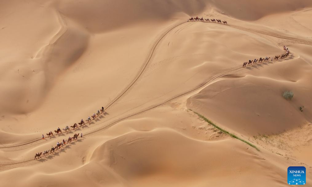 An aerial drone photo taken on Aug. 1, 2025 shows people riding camels at a desert scenic area in Dalad Banner of Erdos City, north China's Inner Mongolia Autonomous Region. Kubuqi desert in Erdos City has entered its peak tourist season in midsummer, attracting numerous tourists from around the country to visit. (Xinhua/Lian Zhen)