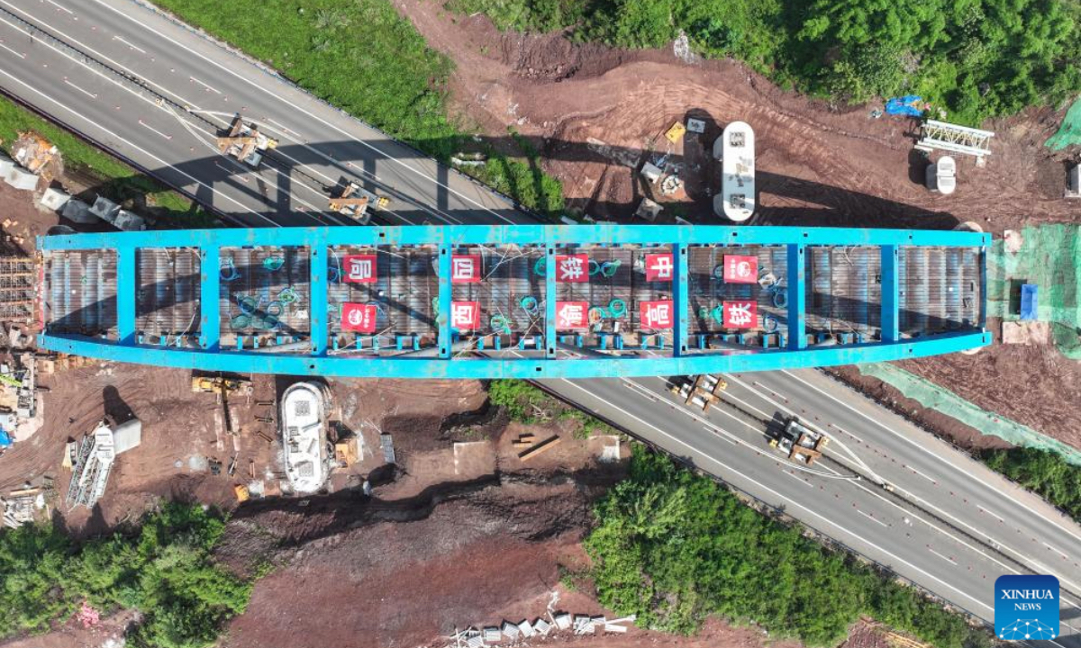 An aerial drone photo taken on July 11, 2025 shows a bridge of the Xi'an-Chongqing high-speed railway over an expressway under construction in Dazhou, southwest China's Sichuan Province. The main body of a bridge of Xi'an-Chongqing high-speed railway over an expressway linking Yingshan and Dazhou in Sichuan Province was smoothly lowered onto its piers on Friday. This marks the successful completion of the incremental launching construction for China's first large-span high-speed railway network arch bridge with tied girders, laying a solid foundation for the timely opening of the Xi'an-Chongqing high-speed railway. The bridge spans 443.1 meters in total length, and the constructed tied-arch bridge section weighs 2,600 tonnes, measuring 147 meters long and 17 meters wide, with an incremental launching displacement of approximately 146 meters over a 10-day construction period. (Xinhua/Wang Xi)