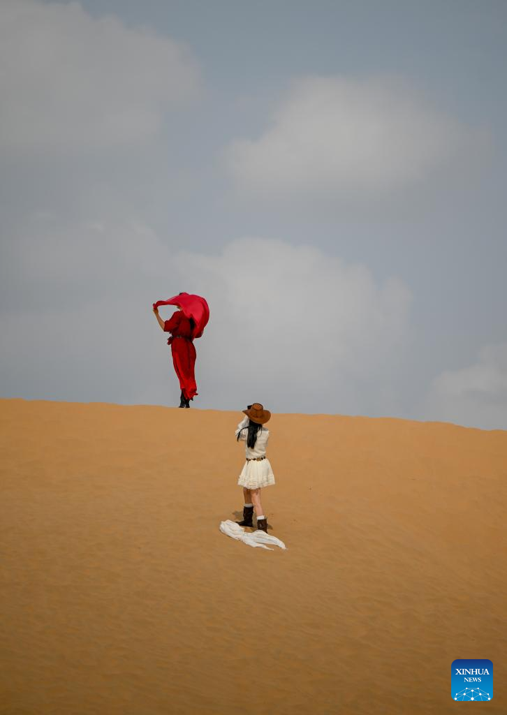A tourist poses for photos at a desert scenic area in Dalad Banner of Erdos City, north China's Inner Mongolia Autonomous Region, Aug. 1, 2025. Kubuqi desert in Erdos City has entered its peak tourist season in midsummer, attracting numerous tourists from around the country to visit. (Xinhua/Lian Zhen)