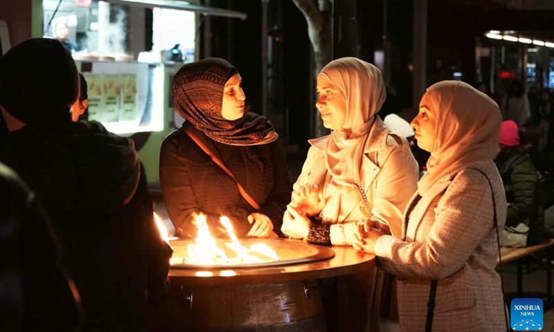 People chat around a fire pit during the Winter in the City event in Canberra, Australia, on July 19, 2025. Wrapped up here on Saturday, the two-week event enlivened Canberra's city center with nightly fire shows, acrobatic performances and interactive musical theatre, creating a vibrant winter festive atmosphere. Besides the entertainment, over 30 food stalls representing cuisines from around the world offered visitors a diverse culinary experience. (Photo: Xinhua)