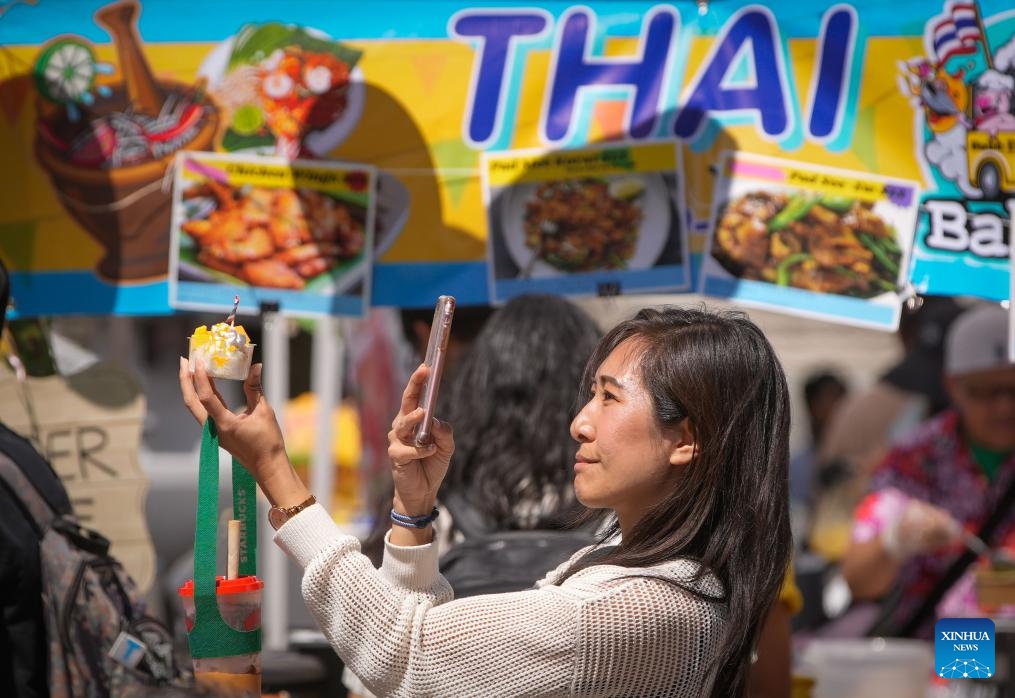A woman takes a photo of her Thai dessert during the 2025 Thai Festival in Vancouver, British Columbia, Canada, July 27, 2025. The annual Thai Festival featured traditional food, music, dance, crafts and cultural performances, highlighting Thailand's rich and vibrant culture.（Photo: Xinhua)