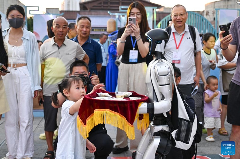 A child reaches for vine tea products served by a robot in Laifeng County of Enshi Tujia and Miao Autonomous Prefecture, central China's Hubei Province, Aug. 1, 2025. Laifeng County has leveraged comprehensive industrial chain development to optimize the business ecosystem for vine tea cultivation. The county has expanded its vine tea plantations to 102,000 mu (about 6,800 hectares), generating an annual output value of 2.253 billion yuan (about 321.4 million U.S. dollars). The industry has lifted household incomes for over 20,000 rural families. Photo: Xinhua