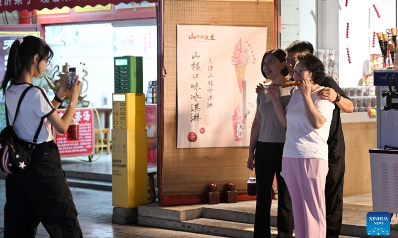 Tourists pose for photos on an ancient cultural street in north China's Tianjin Municipality, Aug. 3, 2025. Local shop-owners have extended operating hours and organized live performances to attract visitors, boosting the summer economy. (Xinhua/Zhao Zishuo)