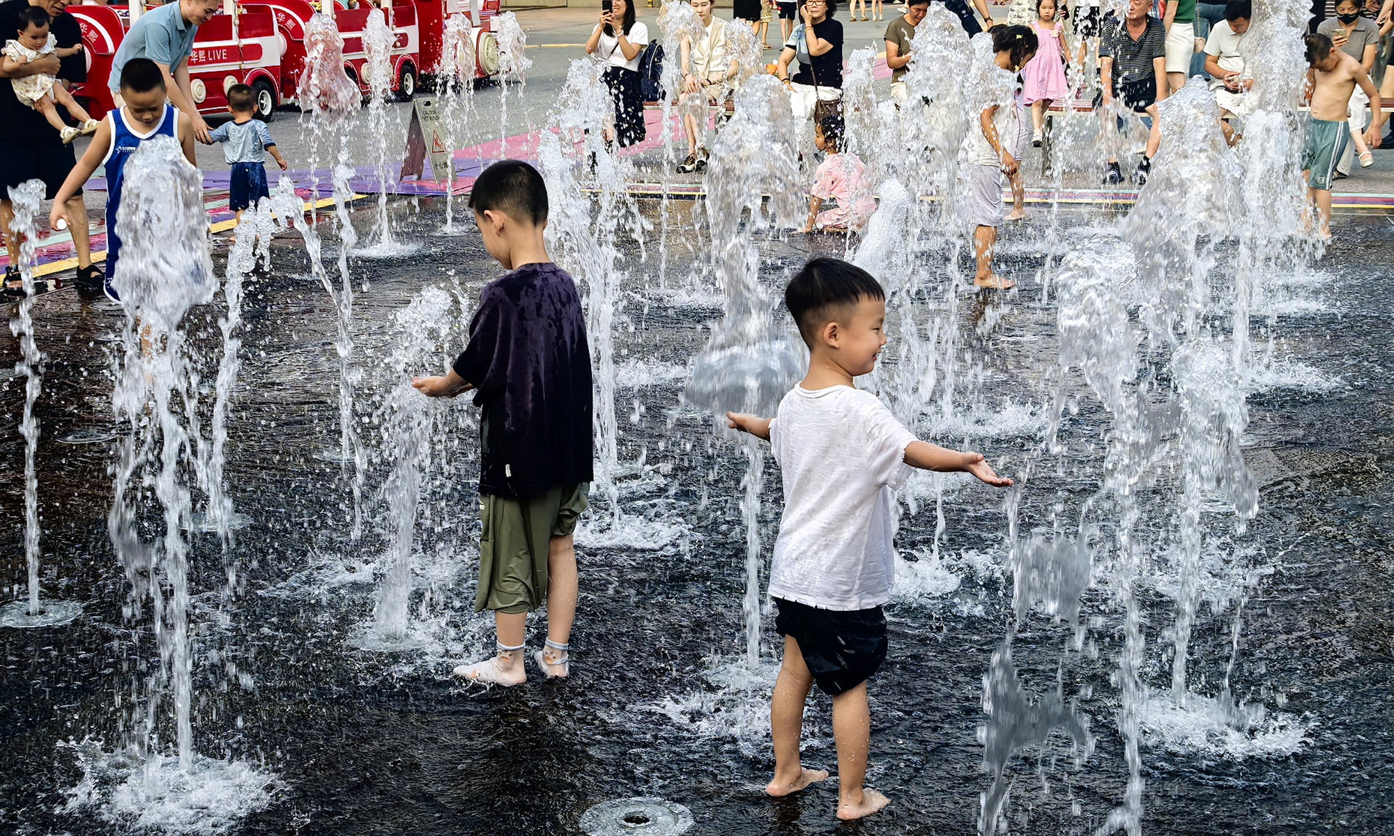 Parents and children cool off by playing in a fountain at the Wukesong commercial block in Beijing, on August 1, 2025.