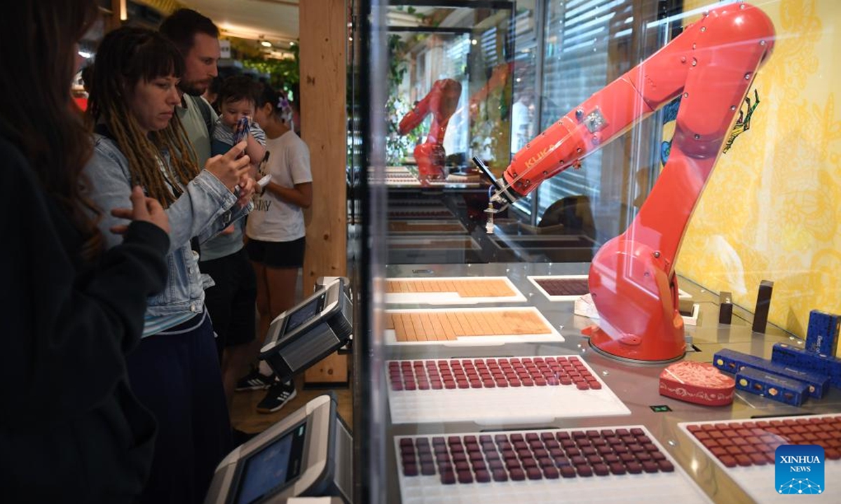 Visitors observe a robotic arm picking up chocolate at Zotter Chocolate Theatre in the town of Bergl, Styria state, Austria, Aug. 6, 2025. Zotter Chocolate Theatre, located in the town of Bergl, Austria's Styria, provides an experience of tasting various flavors and observing chocolate production to all visitors. (Xinhua/He Canling)
