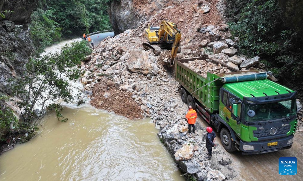 An aerial drone photo taken on Aug. 10, 2025 shows staff members of the transportation department driving an excavator and a truck to move rocks on a road in Baokang County, Xiangyang City, central China's Hubei Province. Recently, affected by continuous heavy rainfall, many roads in Baokang County were blocked. The transportation department quickly carried out rescue and resumed the weather-disrupted traffic. (Photo by Chen Quanlin/Xinhua)