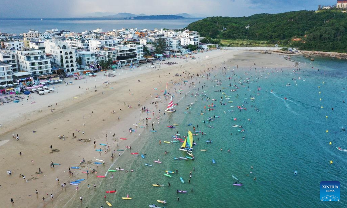 An aerial drone photo taken on Aug. 9, 2025 shows tourists surfing on a beach in Sanya City, south China's Hainan Province. Tourists are flocking to Sanya for the pleasure of surfing during the summer vacation. (Xinhua/Guo Cheng)