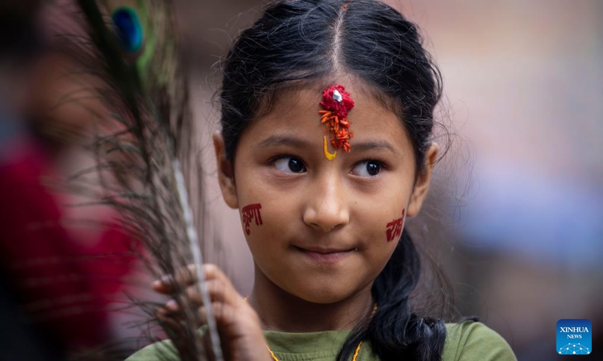 A girl poses for photos with peacock feathers in hand during the Krishna Janmashtami festival in Lalitpur, Nepal, Aug. 16, 2025. (Photo by Hari Maharjan/Xinhua)