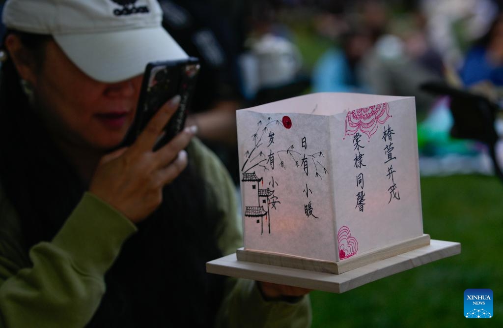 A woman takes photos of her water lantern during the Water Lantern Festival in Coquitlam, British Columbia, Canada, Aug. 16, 2025. The event attracted hundreds of residents and visitors to enjoy the illuminated lanterns and share wishes for hope and joy. (Photo by Liang Sen/Xinhua)