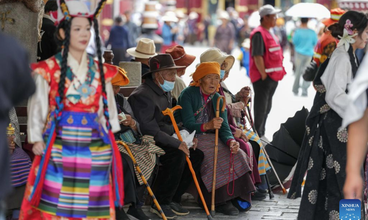 Elder Tibetans rest as a tourist wearing Tibetan costumes poses for photos at the ancient city of Lhasa, southwest China's Xizang Autonomous Region, Aug. 19, 2025. (Xinhua/Jigme Dorje)
