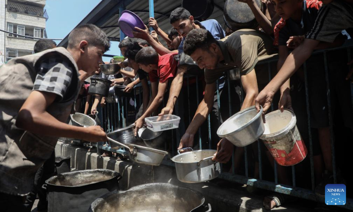 Displaced Palestinians wait to receive free food at a distribution center in Gaza City, on Aug. 18, 2025. (Photo by Rizek Abdeljawad/Xinhua)