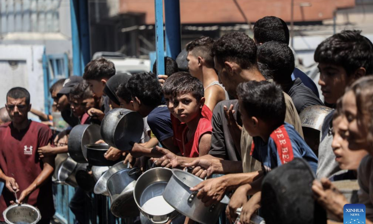 Displaced Palestinians wait to receive free food at a distribution center in Gaza City, on Aug. 18, 2025. (Photo by Rizek Abdeljawad/Xinhua)