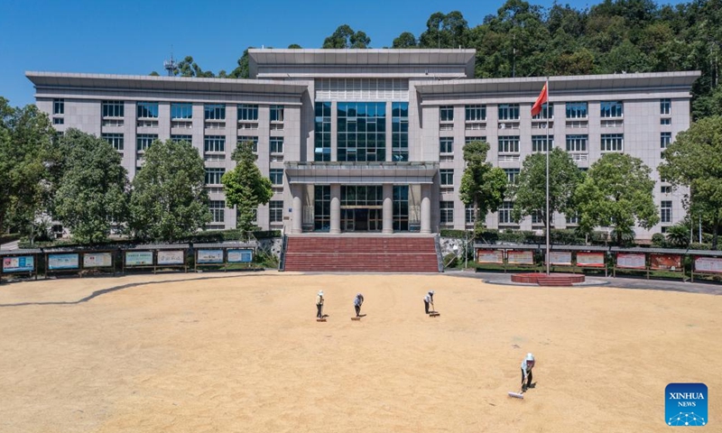 A drone photo taken on Aug. 20, 2025 shows people drying grain at a government compound in Yongchuan District of southwest China's Chongqing Municipality. In recent days, rice in Yongchuan District has entered the harvest season. Local government has provided public areas such as government compounds and cultural squares for farmers to dry grain. (Xinhua/Huang Wei)