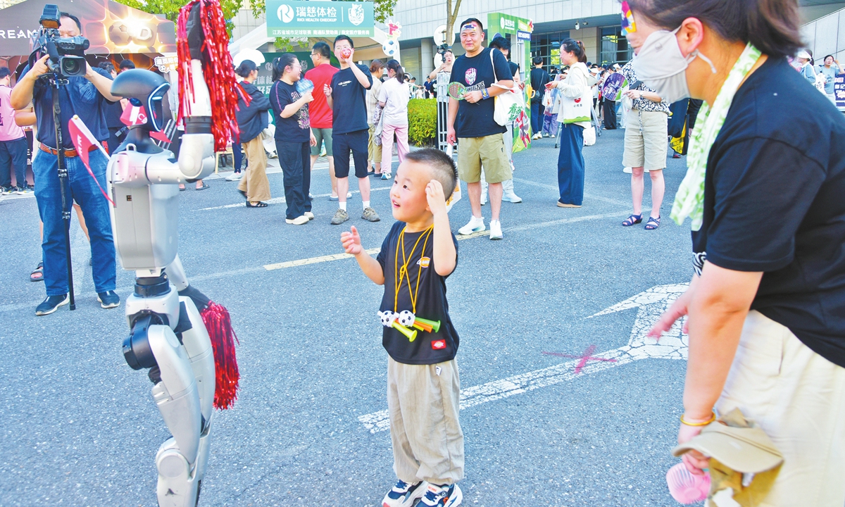 A boy interacts with a humanoid robot outside Nantong's new stadium during the seventh round of Suchao on July 19, 2025. Photo: VCG