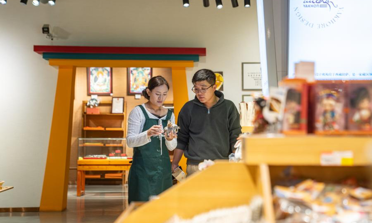 A staff member (L) shows a cultural and creative ornament designed by Yakhore Design Company to a customer at a shop in Lhasa, southwest China's Xizang Autonomous Region, Sept. 29, 2025. (Xinhua/Tenzin Nyida)