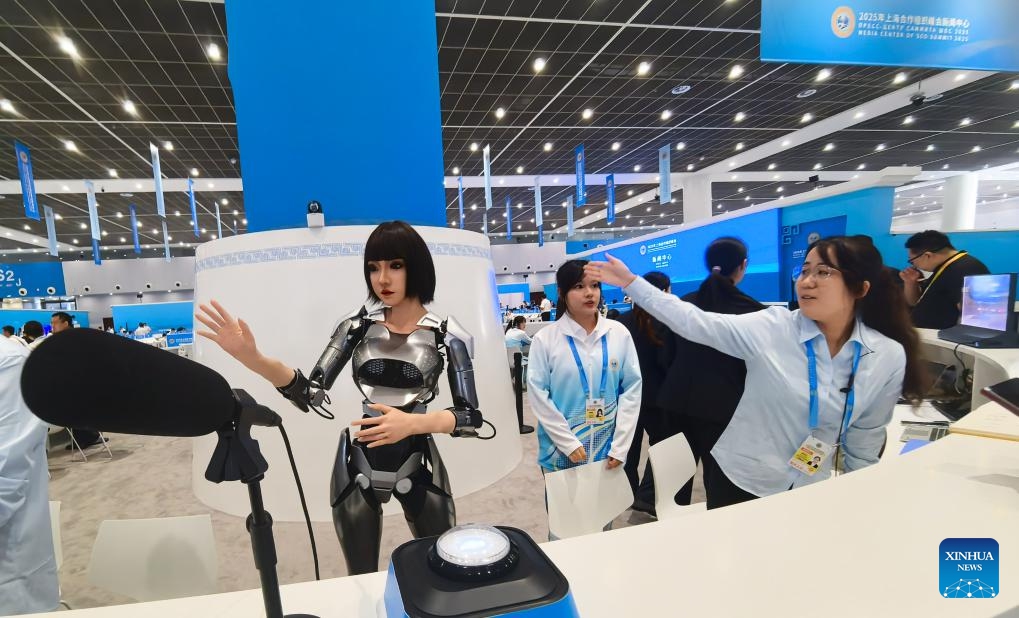 A staff member happens to gesture in sync with Xiaohe, a multimodal interactive robot, at the media center for the Shanghai Cooperation Organization (SCO) Summit 2025 in north China's Tianjin, on Aug. 30, 2025. A variety of robots have attracted numerous eyes at the media center as the SCO Summit 2025 is held in this port city from Aug. 31 to Sept. 1. (Photo: Xinhua)