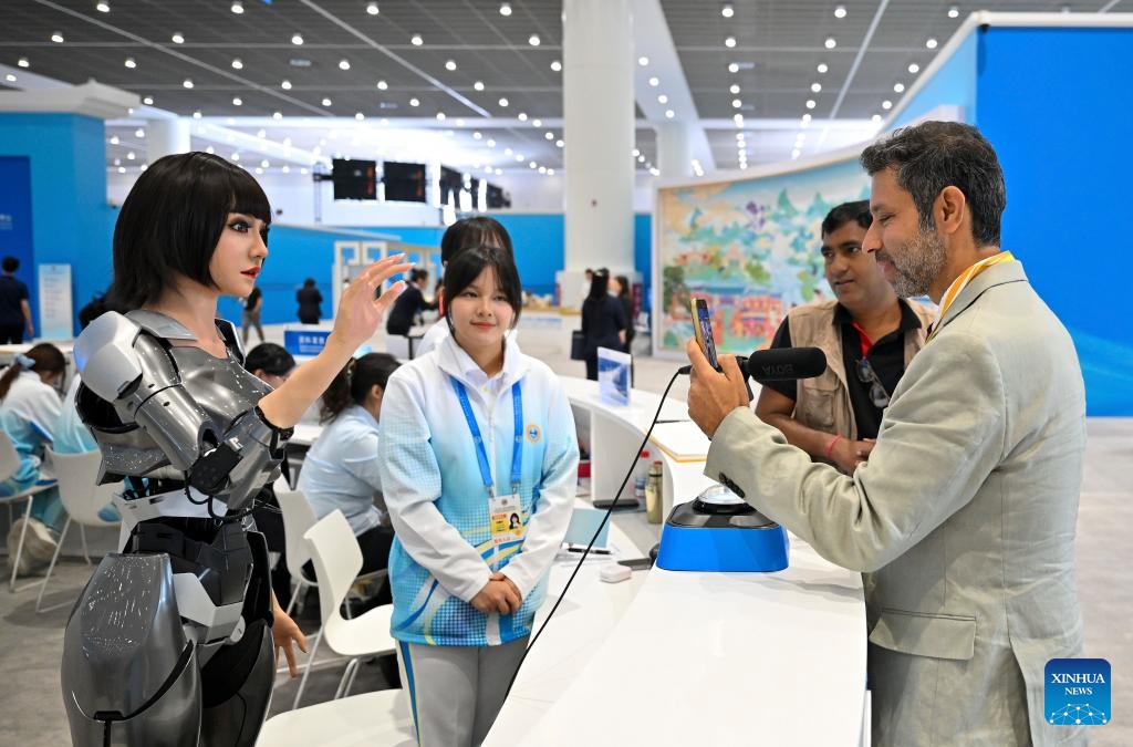 Volunteers serve on the side as a journalist communicates with a multimodal interactive robot at the media center for the Shanghai Cooperation Organization (SCO) Summit 2025 in north China's Tianjin, on Aug. 30, 2025. The SCO Summit 2025 is held from Aug. 31 to Sept. 1 in Tianjin. A team of nearly 1,000 volunteers from local universities provide various service in areas like diplomatic etiquette, emergency response and language services to support the SCO Summit. (Photo: Xinhua)