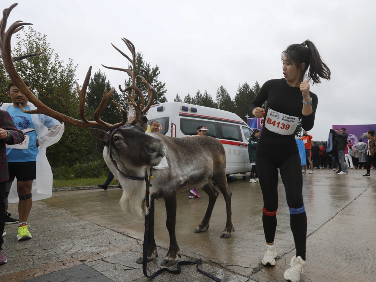 A runner poses for photos with a reindeer raised by people of the Oroqen ethnic group as the Mohe Marathon kicks off at Beijicun, or 
