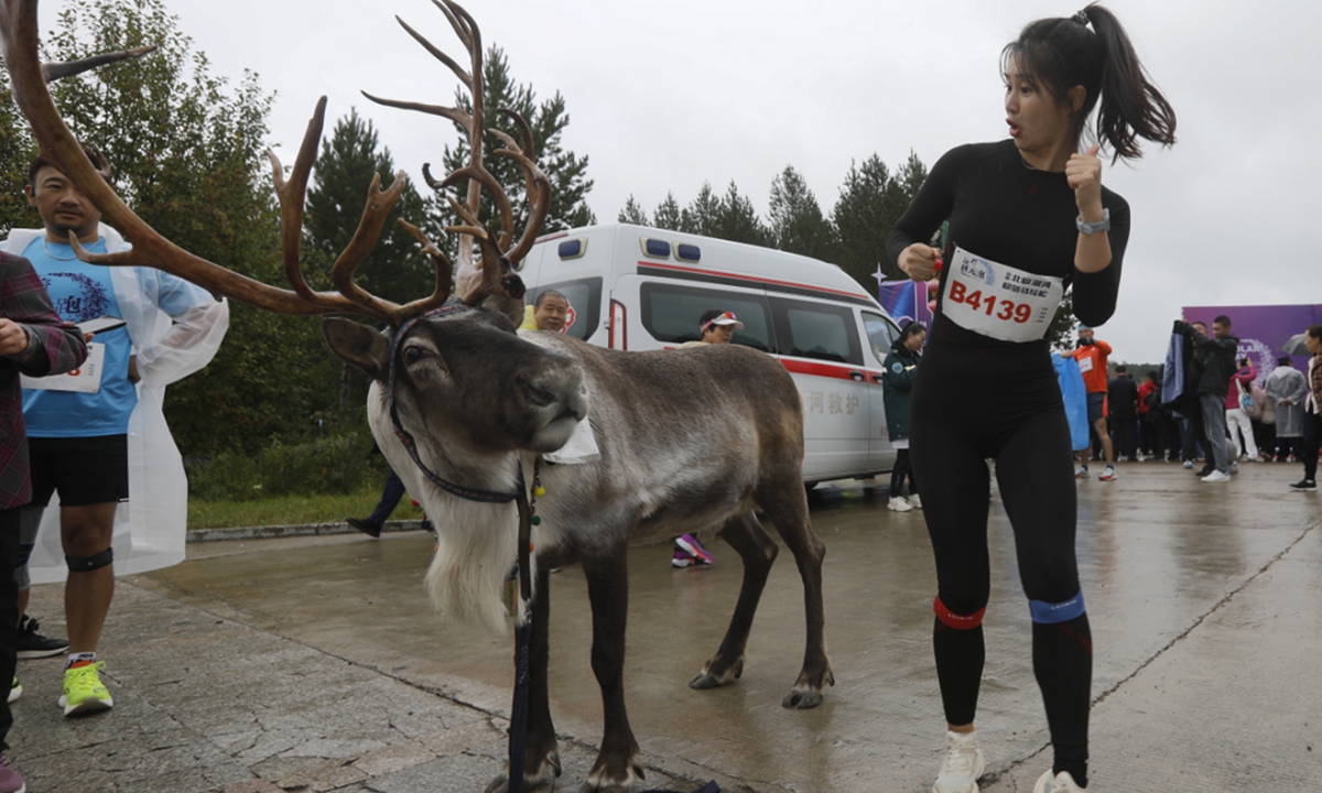 A runner poses for photos with a reindeer raised by people of the Oroqen ethnic group as the Mohe Marathon kicks off at Beijicun, or 