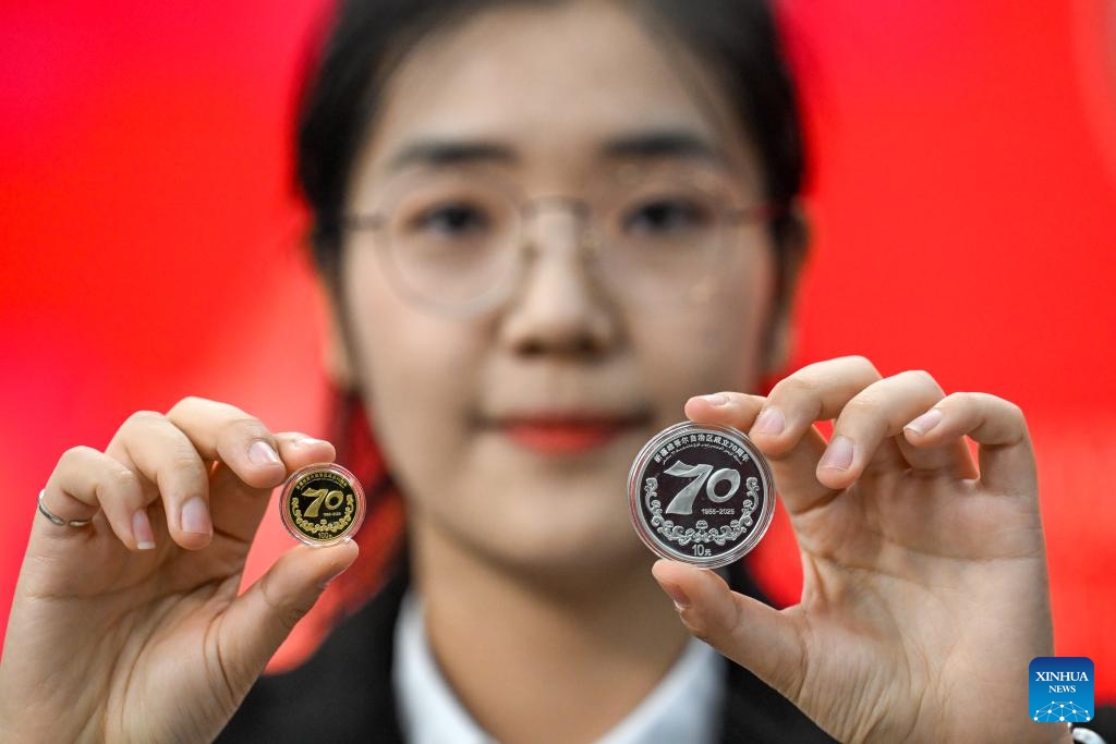 A staffer displays a set of commemorative coins to mark the 70th anniversary of the establishment of Xinjiang Uygur Autonomous Region, in Urumqi, northwest China's Xinjiang Uygur Autonomous Region, Sept. 19, 2025. The People's Bank of China on Friday issued a set of gold and silver commemorative coins to mark the 70th anniversary of the establishment of Xinjiang Uygur Autonomous Region in northwest China. The set, which consists of one gold coin and one silver coin, is legal tender in China. (Xinhua/Ding Lei)
