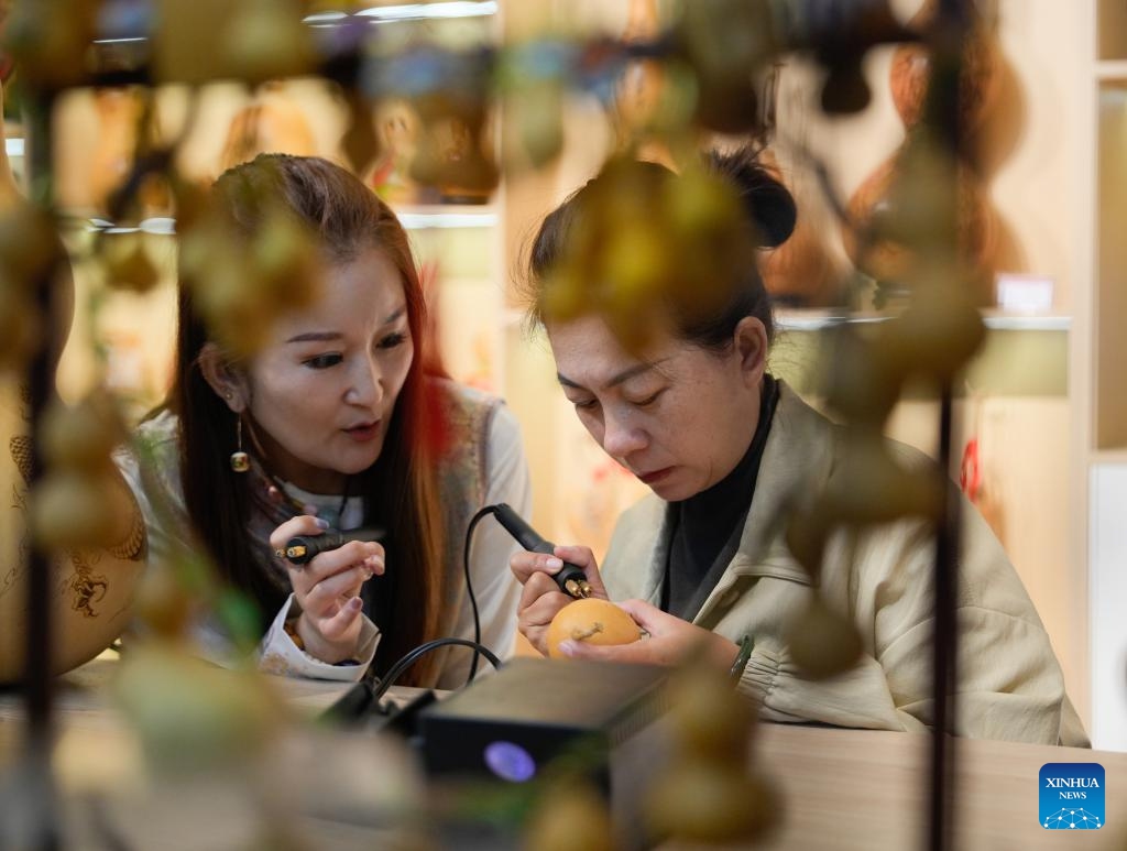 A traditional culture enthusiast (R) learns gourd pyrography following an artisan's guidance at the Emin County memory museum in Emin County, northwest China's Xinjiang Uygur Autonomous Region, Sept. 13, 2025. While showcasing multi-ethnic culture and local history of the county, the museum has attracted many artisans and traditional culture lovers for handicraft exchange. (Photo: Xinhua)