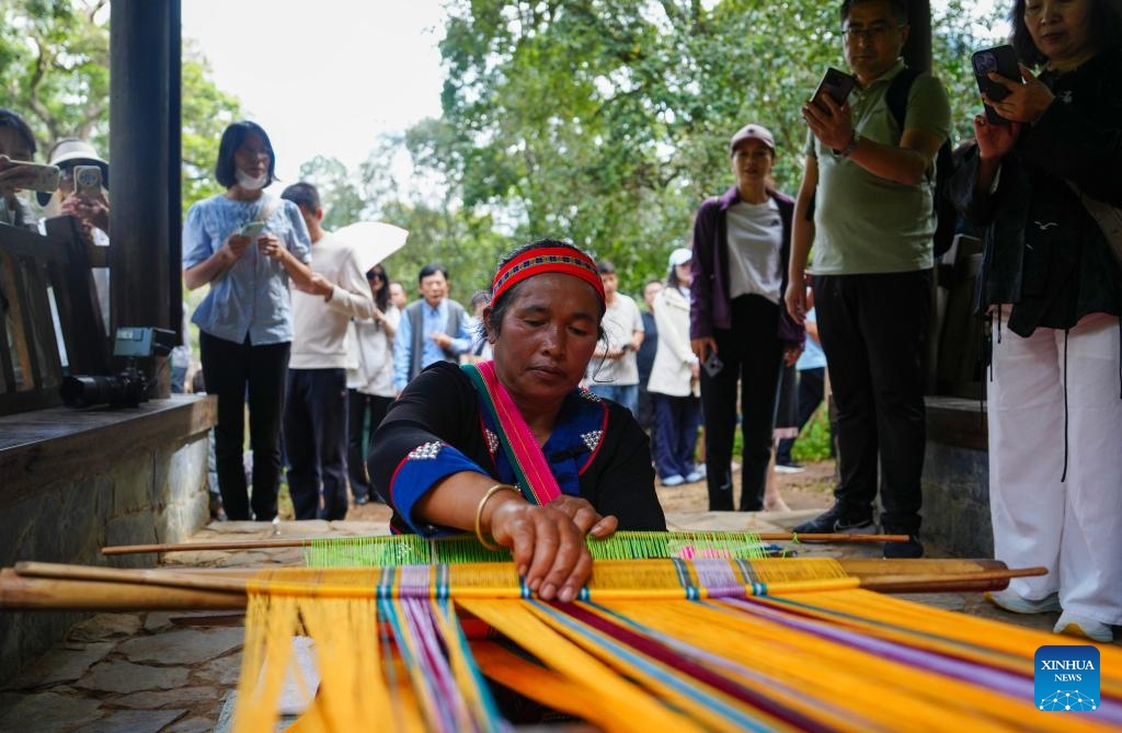A villager displays brocade weaving technique to visitors at an old tea garden on the Jingmai Mountain in Pu'er City, southwest China's Yunnan Province, Sept. 27, 2025. As the world's first tea-themed cultural heritage site, the Cultural Landscape of Old Tea Forests of Jingmai Mountain in Pu'er is witnessing a peak in visits in the autumn day. (Photo: Xinhua)